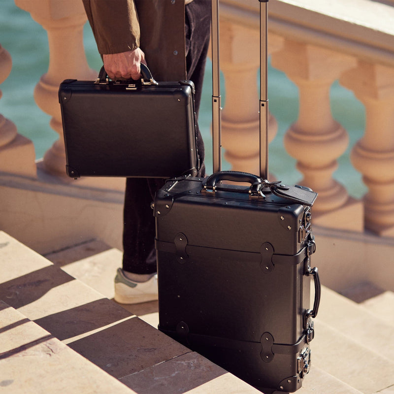 Lifestyle image of male model with The Industrialist fibreboard briefcase and carry-on in  black