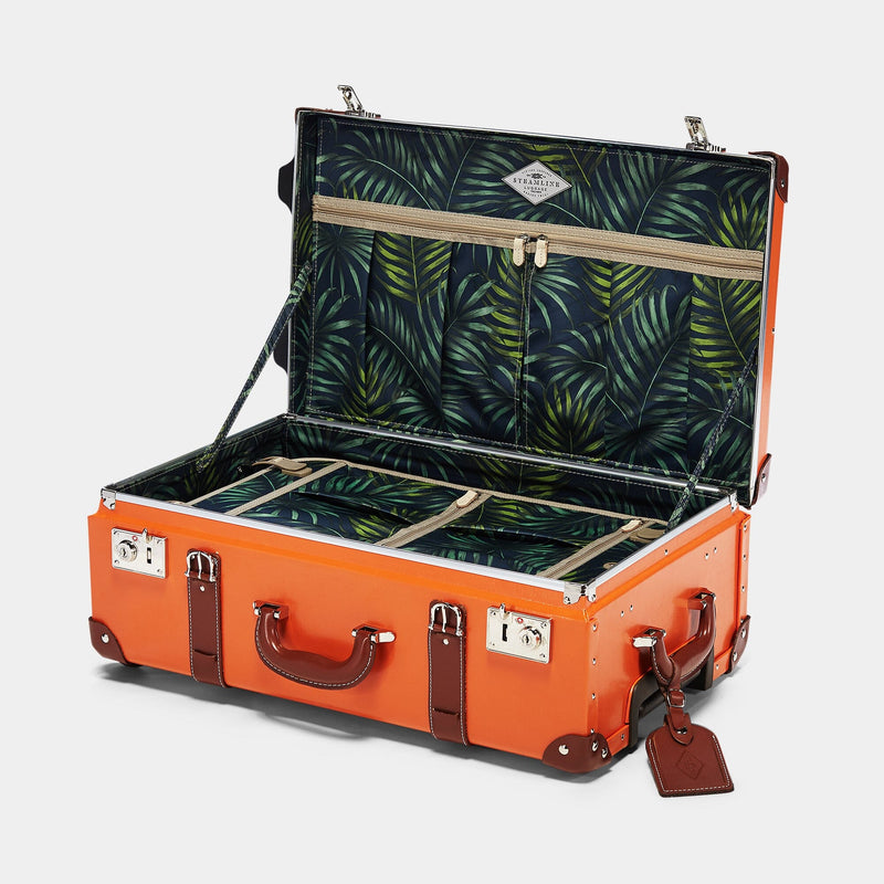 Open product view of the stowaway Anthropologist leather suitcase in orange with green palms printed lining and brown leather luggage tag