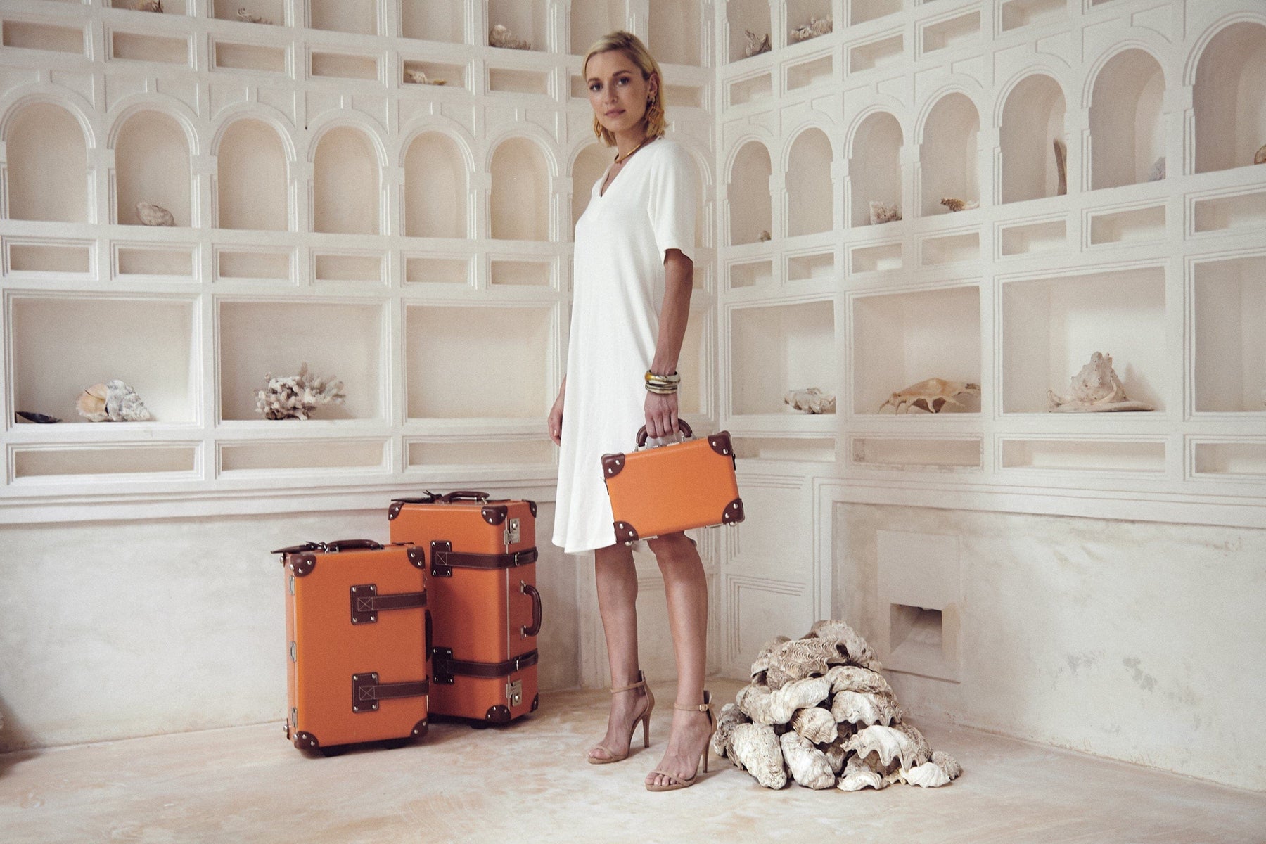 Lifestyle image of model with The Anthropologist leather suitcases in orange