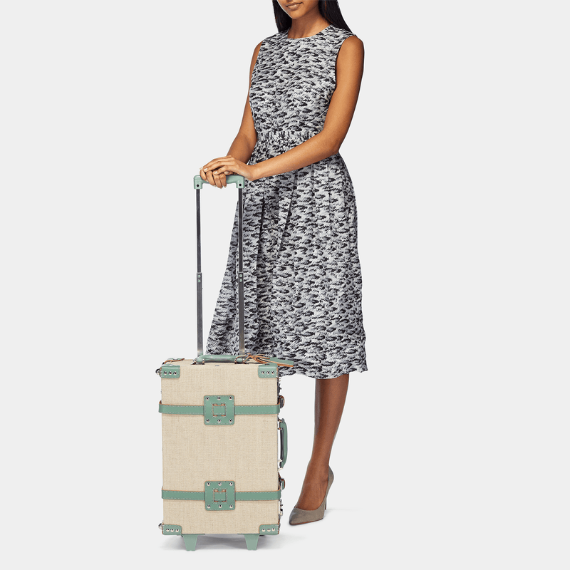 Model with the carry-on Editor linen suitcase with sea green trims and raised handle