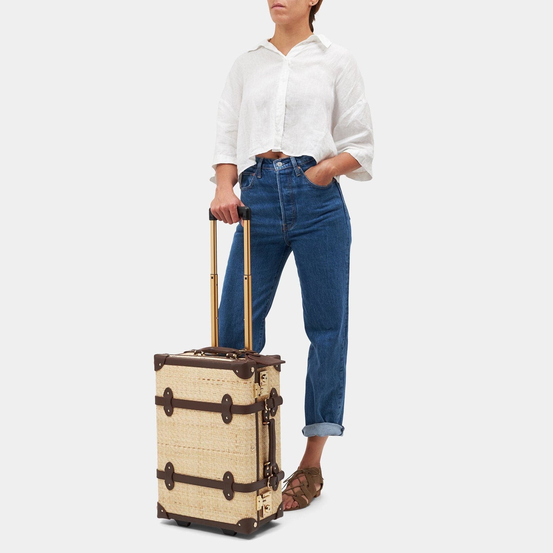 Model with the carry-on Explorer rattan suitcase in natural wicker body and brown trims with raised handle