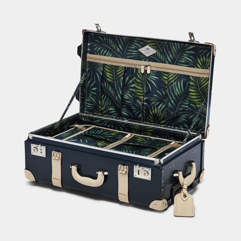 Open product view of the stowaway Anthropologist leather suitcase in navy with green palms printed lining and cream leather luggage tag